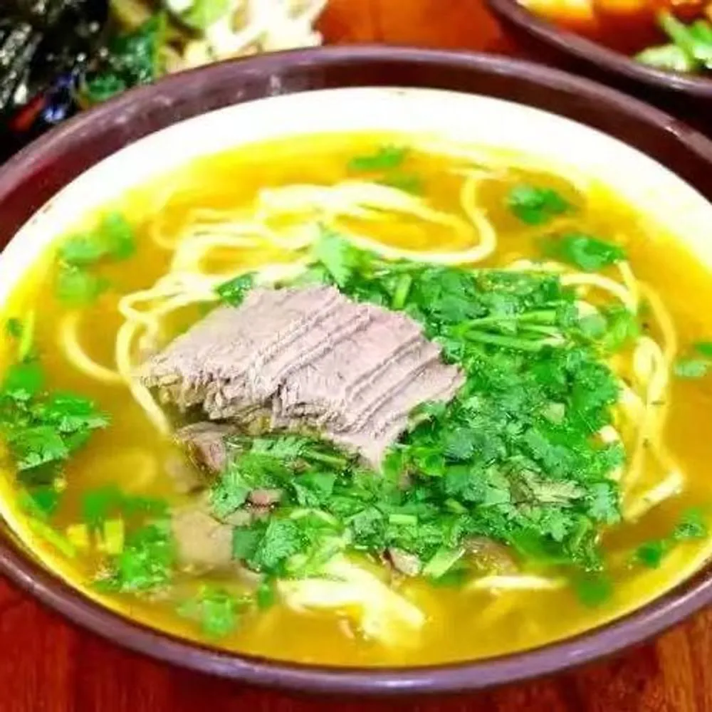 Clear beef noodle soup with sliced beef and fresh cilantro garnish at Noodles + BBQ, a Chinese Restaurant in Los Angeles